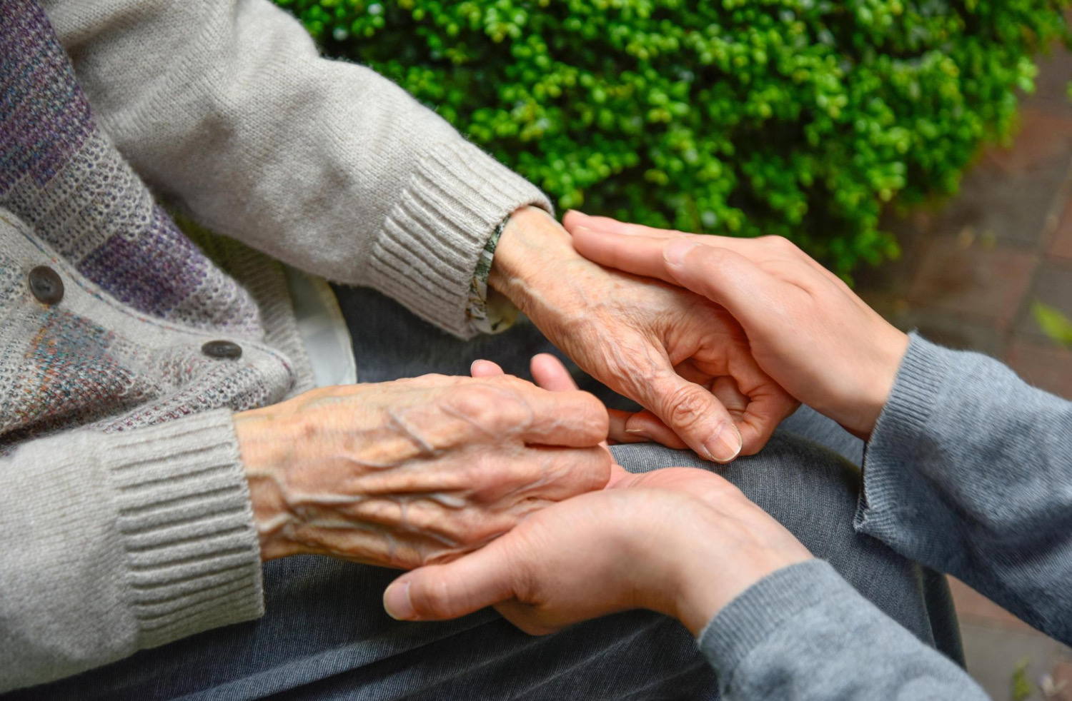 Betreuungskraft hält die Hände einer Seniorin
